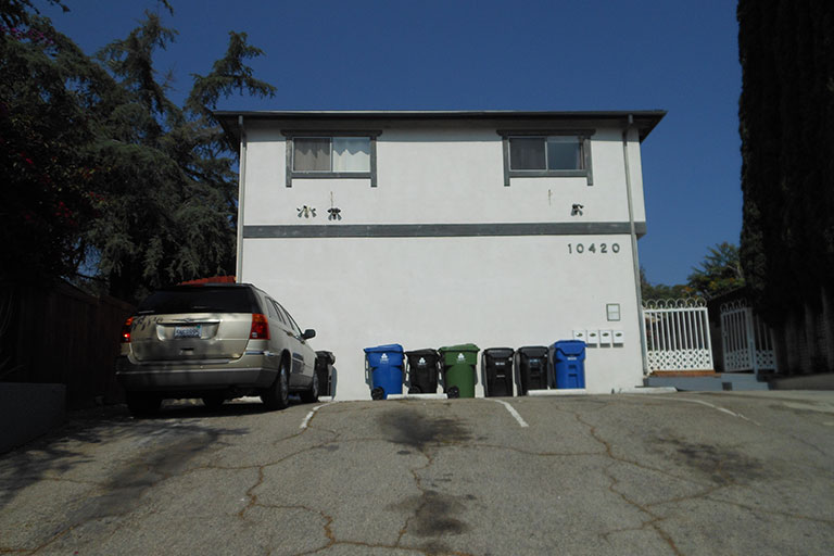 Two-story building with parked car, bins.