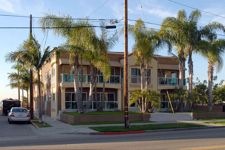 Apartment building with palm trees and car.