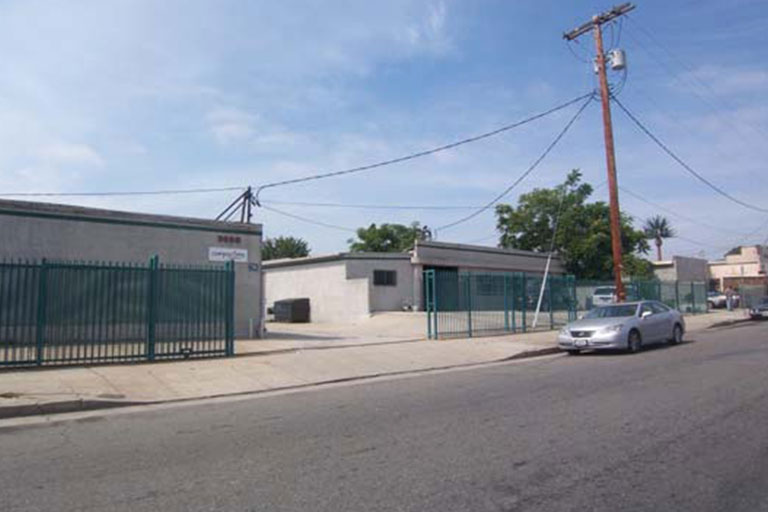Industrial building with green fence and car.
